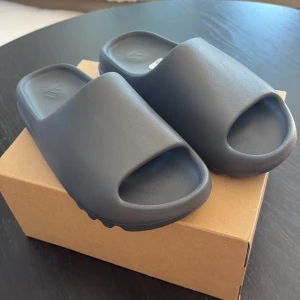 Yeezy slide slate grey - Säljer ett par helt nya yeezy slides i färgen slate grey. Storlek 44,5. Köpta från adidas CONFIRMED appen.