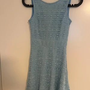 Ljusblå spetsklänning från FB Sister - Supersöt ljusblå kortklänning från FB Sister i spets med v-ringning i ryggen och dragkedja. Klänningen är ärmlös och har ett fint mönster med både blommor och zickzack. Perfekt för sommarens alla tillfällen!