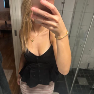 Svart volangig linnetopp med knappar - Supersnygg svart linnetopp med smala axelband och volangig nederdel.  Nypris 329kr, säljes för 250kr