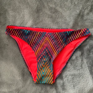 Färgglada bikiniunderdelar med mönster - •Färgglada bikini trosor med ett geometriskt mönster i nyanser av rosa, orange, turkos och svart.  •Trosorna har en röd kant och ett rött foder. •Nya, endast tvättade. •Storlek S. Lindex  🚭Djurfritt och rökfritt hem