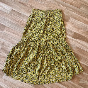 Yellow leopardkjol - Säljer en superfin långkjol i storlek XS. Kjolen är gul med leopardmönster i svart och beige, har volang nertill och elastisk midja med knappar framtill. Perfekt för dig som vill sticka ut med färg och mönster!