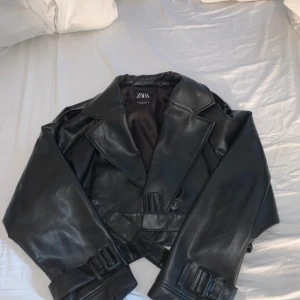 Svart croppad skinnjacka från Zara - Snygg skinnjacka till salu! 🧥✨ Skärp i midjan så du kan anpassa passformen – hur bra?! Perfekt för alla tillfällen och outfits. Hör av dig om du vill veta mer eller lägga ett bud! 😉  Jag har använt den ett fåtal gånger och den är i princip helt ny