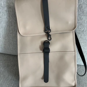 RAINS-rygga – beige & vattentät (passar allt) - Säljer denna snygga och praktiska RAINS Backpack i beige med svarta detaljer – vattentät, stilren och passar perfekt till både vardag, jobb, skola eller resor.  Mått: ca 45 × 30 × 13 cm Unisex – funkar för alla Laptopfack (upp till 15”) Vattentätt material Magnetlås och karbinhake Bekväm att bära med justerbara remmar  Nypris ca 900 kr  