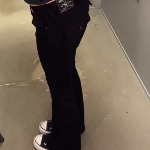 Svarta bootcut jeans från True Religion - Säljer ett par svarta bootcut jeans från True Religion med låg midja. Det är modellen joey. Jeansen är i nytt skick har använt ett fåtal gånger men har fått en defekt längst ner, ett hål som nu är sytt och knappt syns.🙌💞
