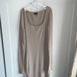 Beige ribbad långärmad klänning - Säljer en beige ribbad klänning från Gina Tricot med lång ärm och  djup urringning. Klänningen är figurnära och har en mjuk, stretchig känsla. 