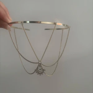 Silvrigt diadem med kedjor och strass - Unikt diadem i silverfärgad metall med tunna kedjor som hänger ner och en dekorativ strassdetalj i mitten. Kedjorna ger en cool och elegant vibe, perfekt för att lyfta din look. Passar dig som gillar statement-accessoarer och vill sticka ut.