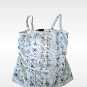 Blommigt linne med spetsdetaljer och knappar från ONLY i storlek Small - Söt ljus linnetopp från ONLY i storlek S med blått blommönster och spetsdetaljer framtill.  Toppen har knappar längs hela framsidan, smala axelband och knytning i ryggen. Den är mer gräddvit i verkligheten, skriv för fler bilder.