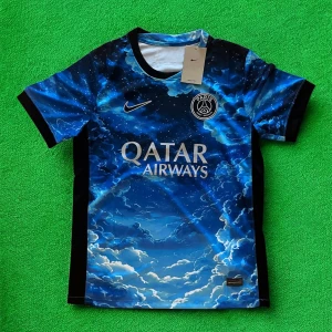 PSG x Nike blå fotbollströja - Snygg PSG fotbollströja från Nike med ett unikt blått moln- och stjärnmönster. Tröjan har korta ärmar, rund hals och Paris Saint-Germain-logga på bröstet. Materialet är lätt och andas, perfekt för träning eller match. Qatar Airways tryck på framsidan.