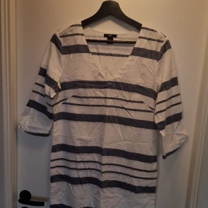 Randig vit och blå klänning H&M - Vit och marinblå randig klänning från H&M i storlek 36. Modellen har v-ringning, trekvartsärm och raka linjer. Perfekt för en avslappnad look. Tillverkad i bomull för en skön känsla. 