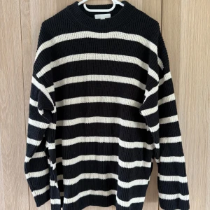 Randig svartvit stickad tröja H&M - Snygg stickad tröja från H&M i svart med vita horisontella ränder. Tröjan har en klassisk rund halsringning och långa ärmar. Perfekt för lager på lager och chill stil. Ribbstickad struktur som ger en skön och avslappnad vibe.