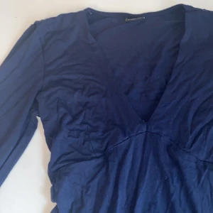 Marinblå omlott topp Gina Tricot - Mörkblå  omlott topp från Gina Tricot i storlek XS. Modellen har lång ärm, djup v-ringning och figurnära passform. Materialet känns mjukt och stretchigt.