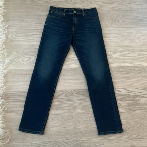 Mörkblå jeans från Polo Ralph Lauren. Ny pris 1995 - Snygga mörkblå jeans från Polo Ralph Lauren med klassisk femficksdesign och guldfärgade sömmar. Jeansen har raka ben och normal passform, tillverkade i mjukt bomullsjeansmaterial. Perfekta för dig som gillar stilrena och tidlösa jeans.