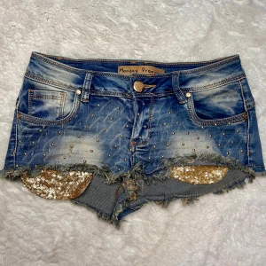 Lågmidjade jeansshorts minishorts vintage med gulddetaljer  - Storlek s. Kan även passa xs. Total längd på ena benet fram: 17cm Midjemått:36cm stretch till 43 alltså extremt stretchiga och passar många midjemått. Köp sker via köp nu. Jag postar inom 24h. Kvar tills markerad såld 