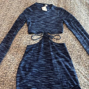 Blå mönstrad klänning från H&M - Supersnygg blå mönstrad kortklänning från H&M Divided med lång ärm och cool snörning i midjan. Klänningen är figurnära med cut out-detalj framtill. Storlek S. Helt ny med prislapp, nypris 199kr.