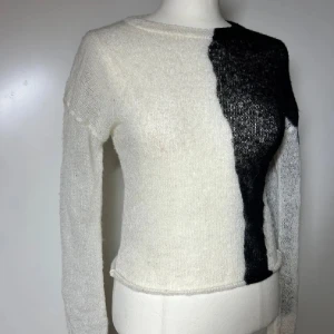Vit och svart stickad topp - Säljer en tunn stickad tröja i vit och svart med coolt asymmetriskt mönster. Tröjan har lång ärm, rund halsringning och är lite croppad i modellen. Perfekt för dig som gillar en unik och trendig look.