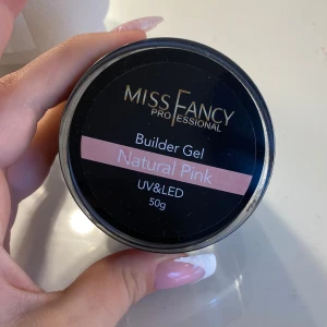 Miss Fancy Builder Gel Natural Pink - Builder Gel i färgen Natural Pink från Miss Fancy Professional. Perfekt för att bygga och förstärka naglar med en naturligt rosa ton. Gelen härdas med både UV- och LED-lampa och kommer i en rund burk på 50g. Mer än hälften kvar, låg viskositet 