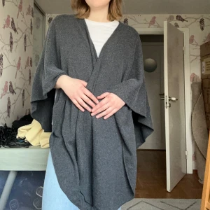Mörkgrå omlottväst i ullmix - Säljer en oversized mörkgrå slängkappa med omlottkänsla.  Mjuk ullmix och har en avslappnad, loose passform som ger en chill vibe. Perfekt att slänga över en t-shirt eller hoodie för extra lager och stil.