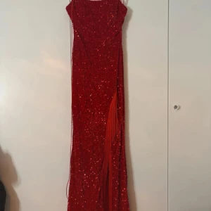 Röd glittrig långklänning med snörning - Säljer en röd långklänning med tunna axelband och glittriga paljetter över hela klänningen. Klänningen har snörning i ryggen och en elegant slits framtill. Perfekt för bal eller fest och ger en riktigt wow-känsla. 