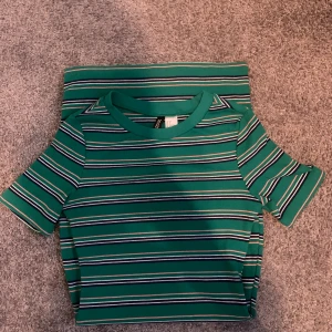 Randig grön klänning  från H&M Divided - Grön ribbad klänning med kort ärm från H&M Divided. Klänningen  har smala horisontella ränder i vitt, marinblått och ljusrosa. Rund halsringning och croppad passform, perfekt för en chill och trendig look. 