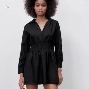 Svart kort klänning från Zara - Svart kort klänning från Zara med lång ärm, v-ringning och krage. Klänningen har smockad midja som ger en snygg siluett och är tillverkad i ett mjukt bomullstyg. Perfekt för dig som gillar stilrena och enkla plagg med en twist. ( är lite liten i storleken så skulle säga att den är mer som en S)💞💞(Har lite smink i nacken men det tvättas självklart bort innan jag fraktar)