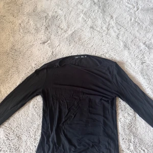 Svart långärmad tröja från Lager 157 - En basic svart långärmad tröja från Lager 157  i mjuk bomull. Tröjan har rund halsringning och en slim passform som sitter snyggt på kroppen. 