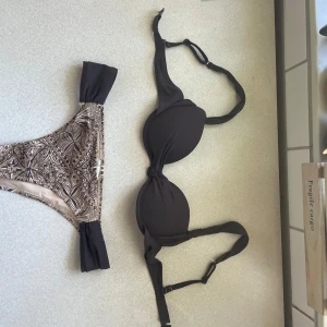 Brun bikini med mönstrad bikiniunderdel - Brun märkesbikini. Storlek 34/36. Använd 2 ggr. Överdelen har ganska små kupor av push-up, och axelbanden är avtagbara. Underdelen är ganska lågmidjad.