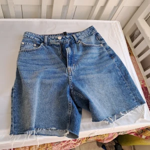 Jeansshorts/jorts från H&M - Blåa jeansshorts från H&M. Halvlånga jorts. Tillverkade i 100% bomull för en skön och avslappnad känsla. Perfekta för varma dagar och enkel att matcha med allt.