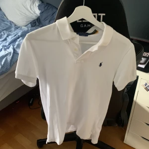 Vit pikétröja från Ralph Lauren - Vit pikétröja från Polo Ralph Lauren i slim fit-modell. Klassisk krage, korta ärmar och knappar framtill. Ikoniska broderade loggan i mörkblått på bröstet. Perfekt för en clean och stilren look. Nypris på denna ligger runt 1299 mitt pris 499 den  är i väldigt bra skick och bara använd cirka 2 gånger storlek är i barns large. Kom privat för mer bilder eller om ni har någon annan tanke.