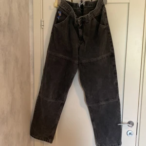 Svarta wide jeans från Polar Skate Co - Säljer ett par svarta jeans från Polar Skate Co med broderad blå och gul figur vid fickan. Byxorna har bred passform, synliga sömmar över benen och är tillverkade i kraftig denim. Perfekta för dig som gillar streetwear och skate.