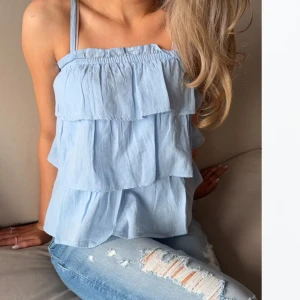 Gina Young Ljusblå volang topp - Supersöt ljusblå linnetopp med tunna axelband och flera lager volanger. Toppen är luftig och har en avslappnad passform, perfekt för varma dagar. Aldrig använd, endast testad - prislapp kvar. Barn storlek 158/164 💕