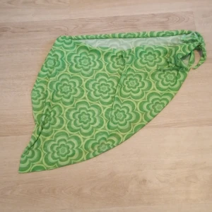 Grön blommig bikini-sarong i storlek L - Köpt på Sellpy så vet inte var den är ifrån. Snygg grön bikini-sarong med retro blommigt mönster i olika gröna nyanser. Tillverkad i stretchigt och lätt material som består av polyester och spandex. Perfekt att knyta runt midjan på stranden eller vid poolen.