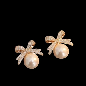 Guldiga örhängen med pärlor och rosett - Supersöta örhängen med gnistrande guldiga rosetter och stora vita pärlor. Rosetterna är täckta av små glittrande stenar som ger extra bling. Perfekta för dig som vill ha en söt och elegant look med en touch av glamour.