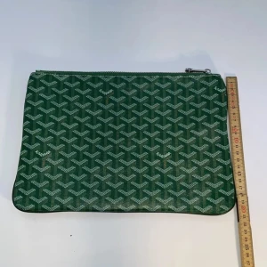 Grön kuvertväska med mönster - Säljer en grön kuvertväska med deras ikoniska grafiska mönster i vitt. Väskan har dragkedja upptill och är tillverkad i slitstarkt material med lyxig känsla. Perfekt för att bära det viktigaste och ge din outfit en exklusiv touch.