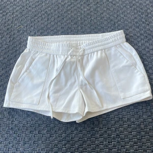 Vita lågmidjade shorts i skinnimitation Gina Tricot - Snygga vita lågmidjade shorts från Gina Tricot i skinnimitation med elastisk midja och snörning. De har två stora fickor fram och en clean baksida. Perfekta för sommarens alla tillfällen när du vill ha en fräsch och trendig look.