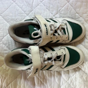 Adidas Forum Low vit/grön sneakers - Snygga Adidas Forum Low sneakers i vitt och grönt skinn med klassiska tre ränder på sidan. Skorna har snörning, kardborreband och en grön yttersula. Perfekt retro vibe och riktigt bekväma för vardagen.