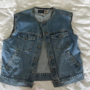 Jeansväst, President Stone - Säljer en blå jeansväst från President Stone med cool flames-patch på ryggen som föreställer en motorcykel i eld. Västen har två bröstfickor med knappar och två sidofickor. Klassisk rak passform och tillverkad i 100% bomull.