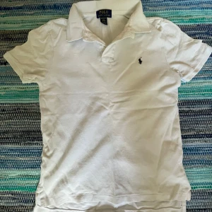 Vit pikétröja från Polo Ralph Lauren - Klassisk vit pikétröja från Polo Ralph Lauren med korta ärmar och broderad marinblå logga på bröstet. Perfekt för sommaren eller när man bara vill vara lite extra snygg. Inga hål eller skavanker på tröjan. Vid frågor bara höra av sig. 