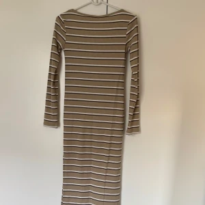 Randig ribbad långklänning  - Snygg långklänning från Lager 157 i ribbad beige trikå med vita, bruna och svarta ränder. Klänningen har en tight passform. 
