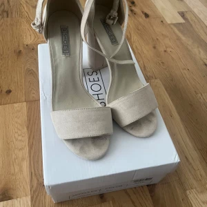 Beige sandaler med blockklack från Shoes - Stilrena beige sandaler med bred blockklack och öppen tå. Skorna har en enkel rem över tårna och justerbar rem runt vristen. Tillverkade i mockaliknande material som ger en mjuk känsla och trendig look. Perfekta för dig som gillar minimalistisk stil.