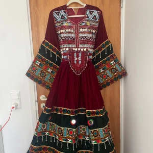 Afgansk klänning - Unik vafgansk långklänning i sammet med breda ärmar, färgglada broderier, små speglar och silverdetaljer. Klänningen har v-ringning, knytning i ryggen och coola mönster i blått, grönt, gult och orange. Perfekt för dig som vill sticka ut med traditionell och färgstark stil.