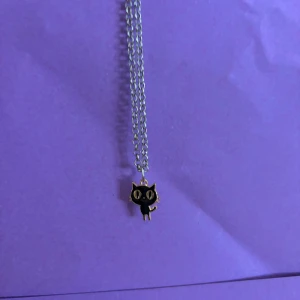 Halsband med svart kattberlock - Sött halsband med en silverfärgad kedja och en liten svart kattberlock med guldiga detaljer. Perfekt accessoar för dig som gillar djur eller vill ha något unikt och lekfullt i din stil.
