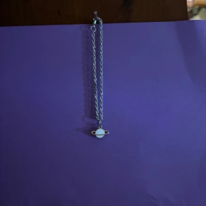Armband med planet-hänge i silver - Snyggt armband med en tunn silverfärgad kedja och ett hänge som föreställer en planet med ringar. Hänget är vitt och silver, perfekt för dig som gillar rymdtema och unika smycken. Passar till alla tillfällen och ger en cool touch till din stil.