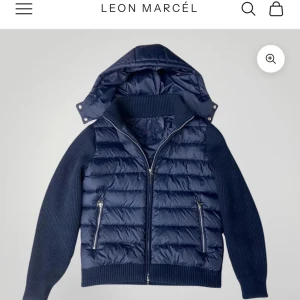 Marinblå pufferjacka från Leon Marcel - Snygg marinblå pufferjacka från Leon Marcel med stickade ärmar och quiltad front. Jackan har avtagbar huva, två dragkedjefickor och ribbade muddar. Jackan är helt ny, säljes pga felköp. Nypris 1350kr.