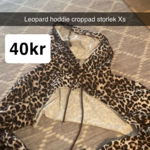 Leopardmönstrad croppad hoodie XS - Säljer en croppad hoodie i leopardmönster med huva och snörning. Tröjan har en loose passform och är perfekt för dig som vill sticka ut. Färgerna är beige och svart, vilket ger en cool kontrast. Passar dig som gillar trendiga och bekväma plagg.