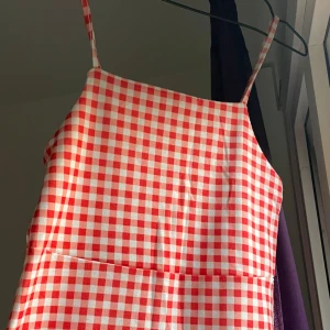 Gingham sommarklänning - Superfin röd och vit rutig klänning med smala axelband och rak halsringning. Klänningen är kort och är perfekt för varma dagar. Materialet känns lätt och svalt, och mönstret ger en retrovibe.