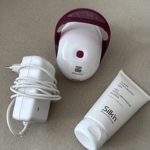 Silk'n Silhouette med hyaluron gel - Silk'n Silhouette är en vit och vinröd apparat för hudvård, tillsammans med en 130 ml tub hyaluron gel. Maskinen har LED-panel undertill och kommer med vit laddare. Perfekt för dig som vill boosta hudens fukt och spänst hemma. Perfekt för dig som vill bli av med celluliter. 