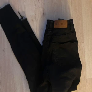 Svarta skinny jeans från NA-KD - Svarta skinny jeans från NA-KD med hög midja och råa benslut. Klassisk femficksmodell i stretchigt jeanstyg, perfekta till sneakers eller boots. Snygg läderpatch med logga bak i midjan.