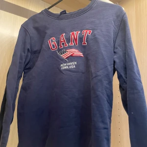 Mörkblå långärmad tröja/sweatshirt från GANT - Snygg mörkblå långärmad tröja från GANT med broderad flagga och text. Klassisk rund halsringning och skön passform, perfekt för dig som gillar preppy college-stil. Passar S och xs. Lite oversize och jätte skön