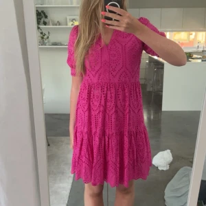 Rosa kortklänning från Y.A.S - Superfin rosa kortklänning från Y.A.S med broderade detaljer och v-ringning. Klänningen har korta puffärmar, volang i kjolen och ett snyggt hålmönster som ger en somrig vibe. Perfekt för dig som vill sticka ut med färg och mönster!