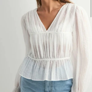 Vit blus med v-ringning och volang - Superfin vit blus i tunn, luftig bomull med v-ringning och långa ärmar. Blusen har lätt rynkade detaljer och volang nedtill som ger en romantisk vibe. Perfekt till jeans eller kjol för en fräsch look. Helt ny aldrig använd! Skriv för mer bilder 